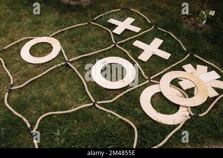 Grande gioco di tic TAC Toe in legno all'aperto su sfondo verde erba. Sfida tra due persone. Divertiti e divertiti all'aperto nel parco. Lei Foto Stock