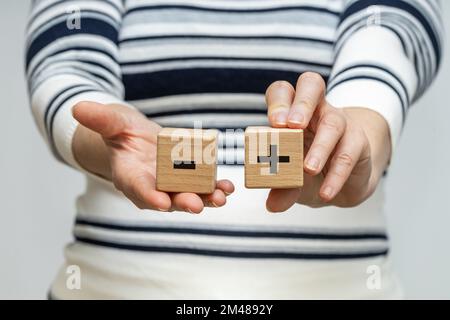 Pro e contro, Una donna tiene blocchi di legno con un simbolo positivo e negativo nelle sue mani, il concetto di pro e contro, su e giù Foto Stock