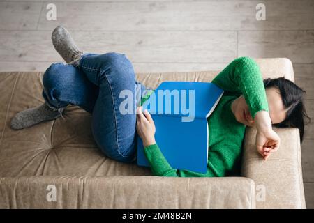 Donna stanca che dorme su un divano con blocco note, concetto di overwork. Foto Stock