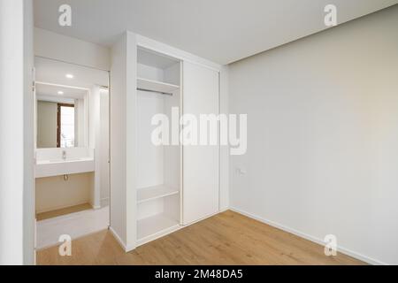 Camera luminosa e spaziosa con pavimenti in parquet e armadio a muro per vestiti e lenzuola. Una porta aperta dalla camera che conduce ad un bagno con un Foto Stock