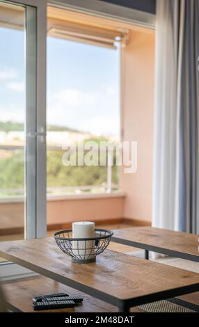 Tavolino da caffè in legno sullo sfondo di un'ampia porta aperta che conduce ad uno spazioso balcone. Sul tavolo c'è una candela bianca aromatica in metallo Foto Stock