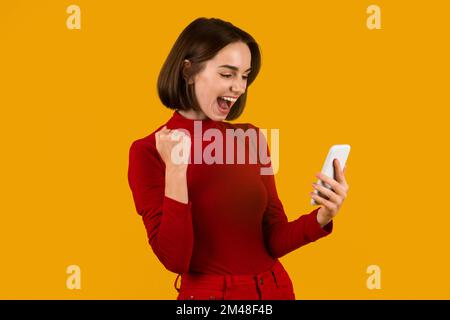 Felice giovane donna che celebra il successo, tenendo il telefono delle cellule Foto Stock