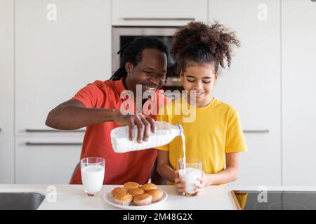 Happy Black papà e figlia mangiano muffin e latte in cucina Foto Stock