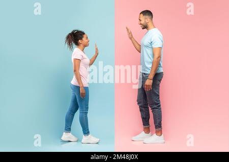 Vista laterale del giovane uomo e della donna neri che si ondeggiano l'uno verso l'altro, in piedi su sfondo rosa e blu dimezzato Foto Stock