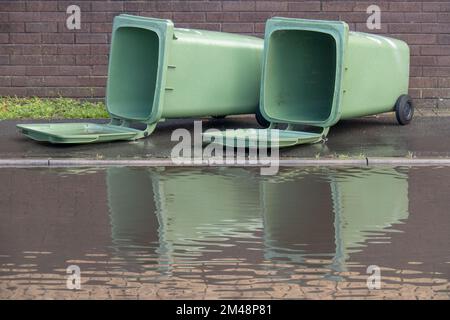 Due grandi bidoni verdi per rifiuti, sdraiati in UK Street, con grandi pozzanghere e acqua allagata. Dopo la tempesta Foto Stock