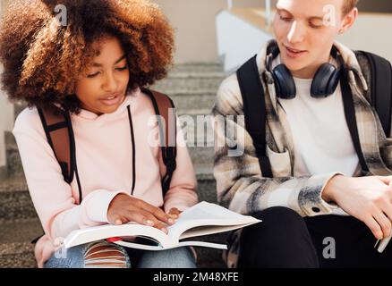 Ragazza e ragazzo seduti insieme su una scala per preparare i compiti a casa Foto Stock