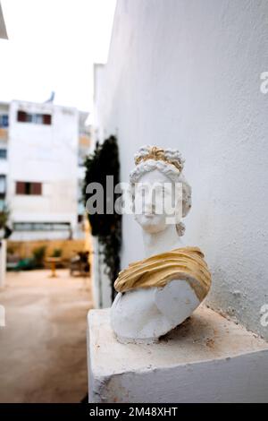 Antico busto di testa di donna contro il muro grigio. Statua storica in abito dorato himation. Antica faccia femminile su sfondo chiaro. Foto di alta qualità Foto Stock