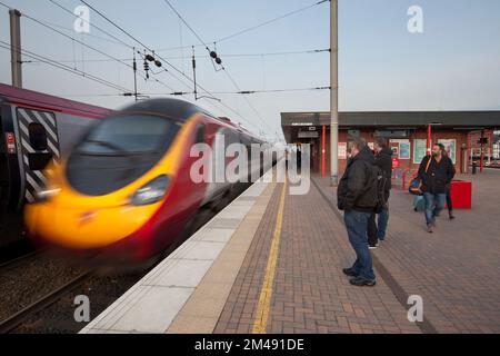 Virgin Train arrivo alla stazione ferroviaria di Wigan North Western con i passeggeri in attesa sulla piattaforma della stazione ferroviaria dietro la linea gialla Foto Stock