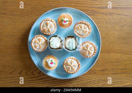 Mince torte con motivi di fiocco di neve e torte di tazza con foglie di agnello commestibili e bacche e alberi di Natale su un piatto blu su un tavolo di legno di quercia Foto Stock