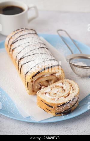 Piatto blu con delizioso rotolo di pan di Spagna e una tazza di caffè su un tavolo bianco Foto Stock