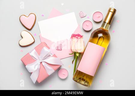 Lettera bianca con rosa, bottiglia di vino, biscotti e omaggio su sfondo grigio. Festa di San Valentino Foto Stock