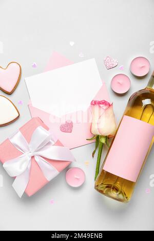 Lettera bianca con rosa, bottiglia di vino, biscotti e omaggio su sfondo grigio. Festa di San Valentino Foto Stock