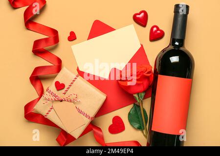 Lettera bianca con rosa, bottiglia di vino, regalo e cuori su sfondo beige. Festa di San Valentino Foto Stock