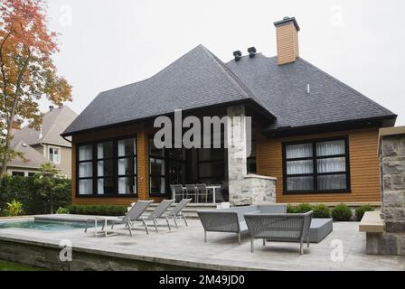 Vista posteriore di una casa in stile cottage decorata con tavole di legno e pietra grigia tagliata in grigio con giardino all'inglese in autunno. Foto Stock