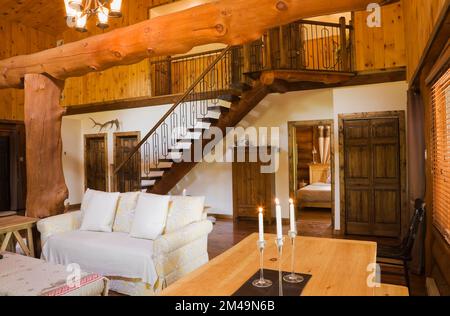 Lungo tavolo da pranzo in legno con candele accese in sala da pranzo e divano in soggiorno all'interno di casa in tronchi, Quebec, Canada, questa immagine è proprietà rilasciata. TAZZA Foto Stock