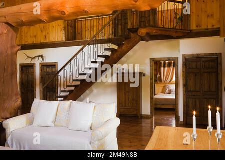 Lungo tavolo da pranzo in legno con candele accese nella sala da pranzo e divano nel soggiorno all'interno di una casa in legno. Foto Stock