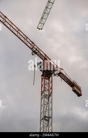 Sagome di gru edili e edificio residenziale incompiuto contro l'alba sopra la città. Edilizia abitativa, condominio costruzione di nuovi edifici residenziali. Sullo sfondo del cielo del tramonto. Foto Stock