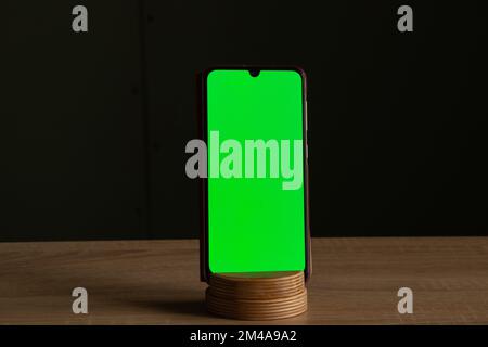 il telefono touchscreen con schermo verde si trova su un piedistallo su un tavolo di legno Foto Stock