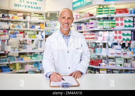 Dimmi i tuoi sintomi e troverai una soluzione garantita. Ritratto di un farmacista maturo che scrive su una clipboard in un chimico. Foto Stock