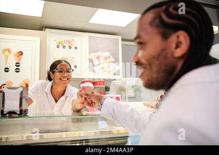 Lavoratore amichevole che serve una terrina di gelato a un cliente Foto Stock