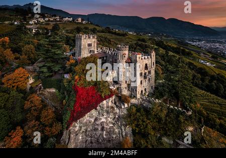 Merano, Italia - veduta aerea panoramica del famoso Castello di Brunnenburg (Castel Tirolo) con la città di Merano, le Dolomiti italiane e il sole colorato Foto Stock