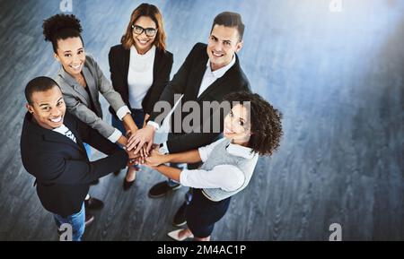 Una cosa che non ci manca è la motivazione della squadra. Colpo ad angolo alto di un gruppo di uomini d'affari che uniscono le loro mani in una huddle. Foto Stock