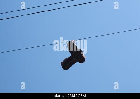 le sneakers sporche appendono su un filo su un palo contro un cielo blu Foto Stock