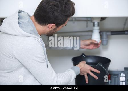 man che fissa un tubo che perde sotto il lavandino Foto Stock