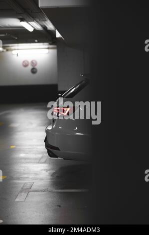 Una foto verticale di un'auto bianca dietro il muro parcheggiato nel garage del parcheggio Foto Stock