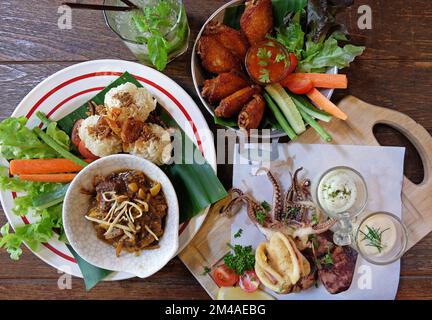 Riso appiccicoso fritto servito con curry della Thailandia settentrionale, ali di pollo e calamari fritti in pastella Foto Stock
