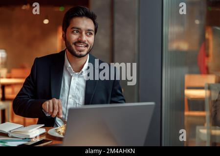 Uomo d'affari indiano che mangia il pranzo durante la pausa dopo il lavoro nel caffè e guardando la finestra Foto Stock