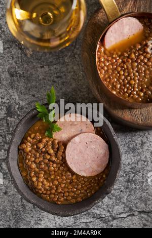 Vista dall'alto di ciotole rustiche con gustosa zuppa di lenticchie con prezzemolo e fette di salsiccia poste su un tavolo di marmo con vino durante il pranzo Foto Stock