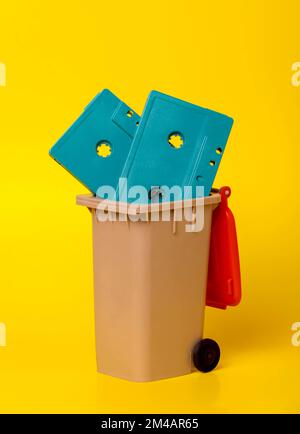 Cassette con nastro in plastica blu retro in contenitore marrone con coperchio rosso posizionato su sfondo giallo brillante Foto Stock