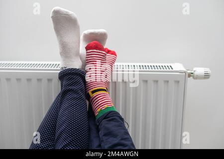 Madre e bambino che scalda i piedi vicino al riscaldatore a casa, primo piano Foto Stock