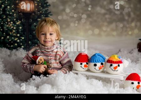 Carino bambino, con il giocattolo lavorato a maglia, giocando nella neve con colorati pupazzi di neve, sorridendo felicemente Foto Stock