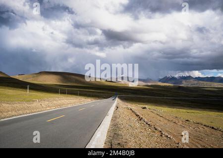 La strada attraversa l'altopiano tibetano con montagne innevate sullo sfondo. Regione autonoma del Tibet. Cina. Foto Stock