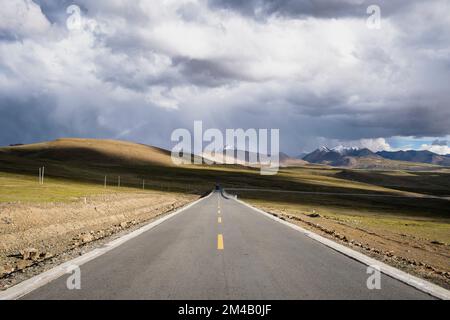 La strada attraversa l'altopiano tibetano con montagne innevate sullo sfondo. Regione autonoma del Tibet. Cina. Foto Stock