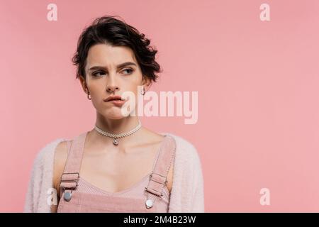 donna offesa in collana perla mordente labbro e guardando lontano isolato su rosa Foto Stock