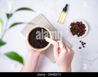 Cura della pelle domestica. Una giovane donna mescola una scab di caffè fatta in casa con l'olio di capsule riciclate. Vista dall'alto e disposizione piatta Foto Stock