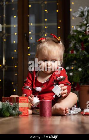 Bella bambina di un anno con capelli biondi giocare regali di Natale. Bokeh ghirlande. Bambini e Capodanno Foto Stock