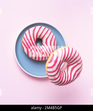 Due ciambelle rosa smaltate che volano in piatto blu su sfondo rosa. Concetto di levitazione cibo . Vista dall'alto Foto Stock