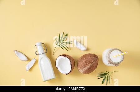 Concetto sano piatto di posa. Bottiglie di latte vegano, fette di cocco e ramo di palma su sfondo giallo. Vista dall'alto e immagine dello spazio di copia Foto Stock