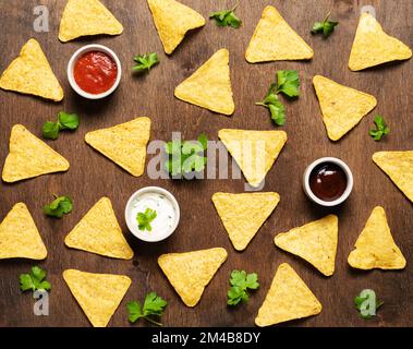 Piatto adagiare con nachos di patatine di mais con salsa di salsa e formaggio e erbe fresche su fondo di legno scuro. Concetto modello cibo messicano. Vista dall'alto. Foto Stock