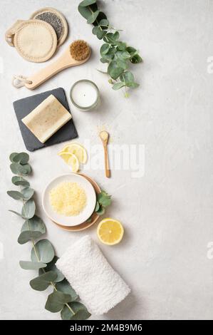 Piatto stendere il sale marino giallo organico con limone, sapone, pennello, spugna e ramificazione di eucalipto su uno sfondo bianco testurizzato. Il concetto di spa e welln Foto Stock