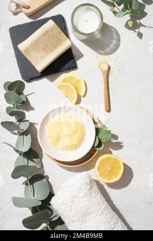 Piatto stendere il sale marino giallo organico con limone, sapone, asciugamano, pennello e ramificazione di eucalipto su uno sfondo bianco testurizzato. Il concetto di spa e wellnes Foto Stock