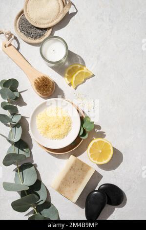 Piatto stendere il sale marino giallo organico con limone, sapone, pietra da massaggio, pennello, spugna e ramo di eucalipto su uno sfondo bianco testurizzato. Il concetto di Foto Stock