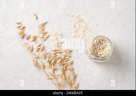 fiocchi di avena in un vaso con brunch secco di avena su uno sfondo bianco testurizzato. Prodotto grezzo e vegano. Cibo naturale. Vista dall'alto e spazio di copia. Foto Stock