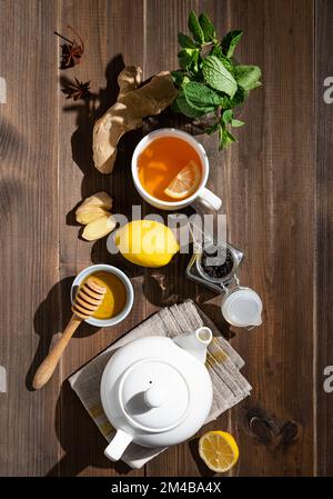 Sistema immunitario booster - piatto tè con zenzero, miele, limone, menta e spezie su uno sfondo di legno scuro con ombra dura. Il concetto di sano Foto Stock