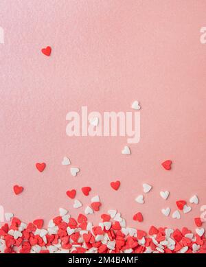 i confetti a forma di cuori rossi e rosa sono sparsi su uno sfondo rosa lucido. Concetto del giorno di San Valentino, del giorno della madre, del giorno di nozze. Vista dall'alto Foto Stock