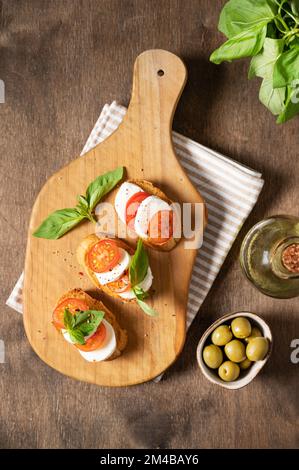 Sandwich caprese con pomodori freschi, mozzarella e basilico fresco e pane tostato su un tagliere con spezie e olio d'oliva su un backgrou di legno Foto Stock